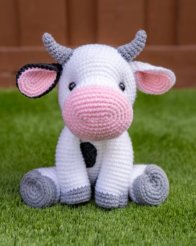 Black and white crocheted cow stuffed animal sitting on grass