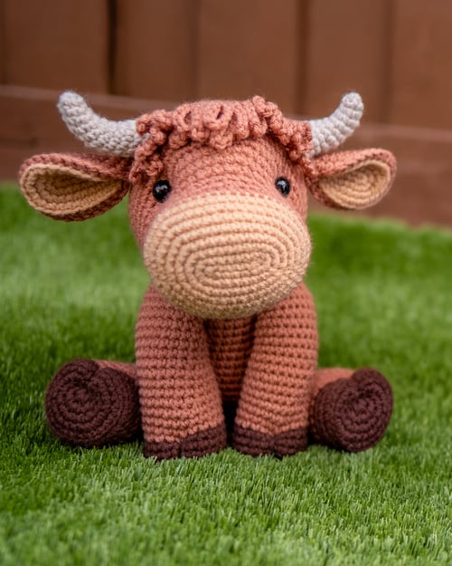 Brown crocheted highland cow stuffed animal sitting on grass